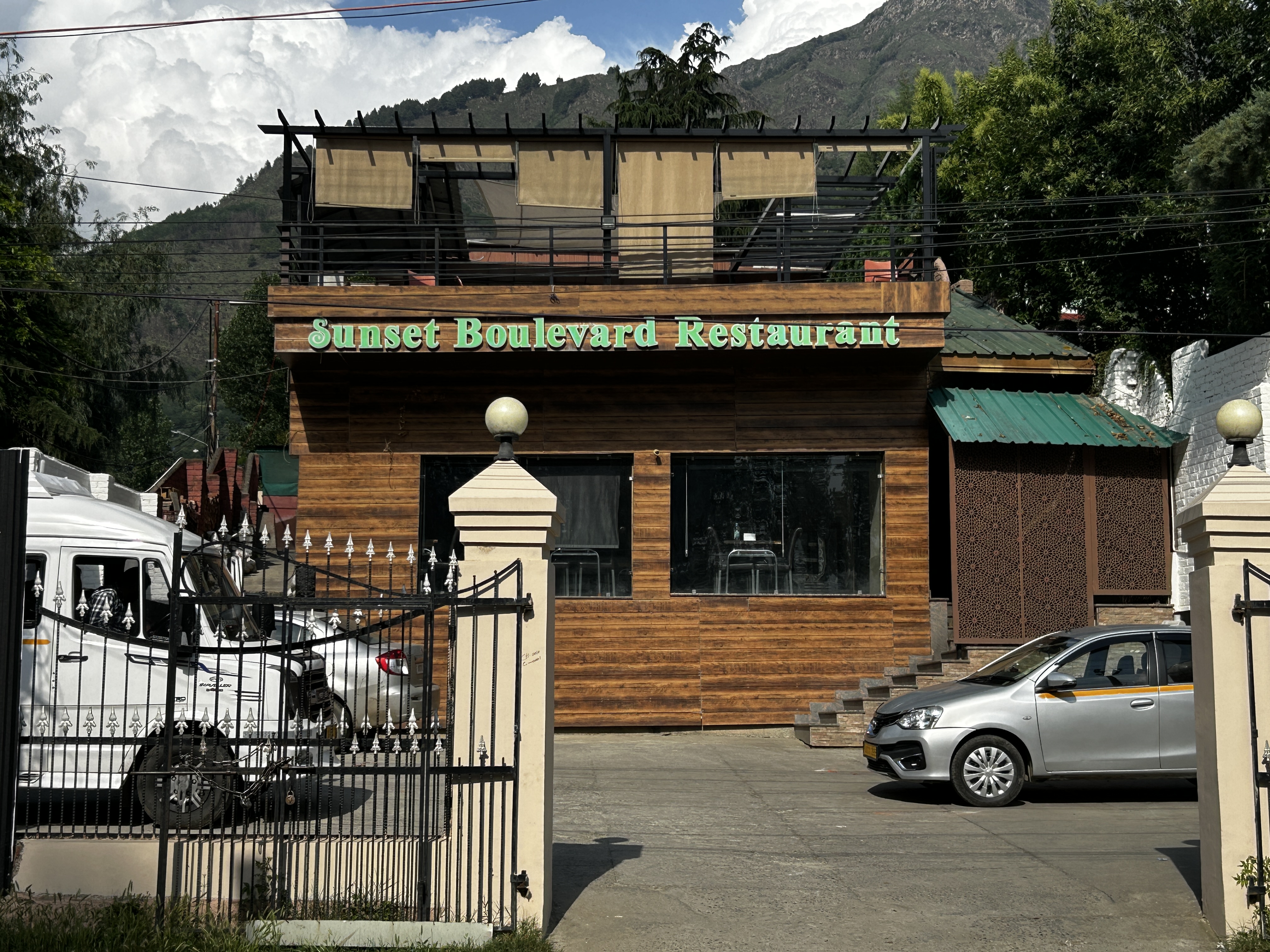 Sunset Boulevard Restaurant exterior - wooden facade with rooftop terrace, surrounded by trees and the Zabarwan mountains, Nishat, Srinagar